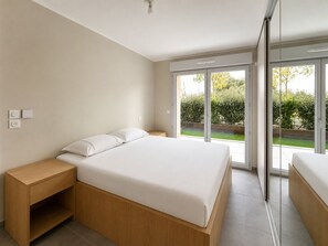 Ein modernes Schlafzimmer mit einem großen Bett, einem Nachttisch aus Holz und einer Schiebetür zu einem Garten.
