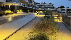 Um edifício residencial com vários andares, varandas, área ajardinada com plantas e um caminho pavimentado.