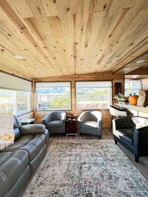 Ein gemütliches Interieur mit Holzbalkendecke, einem Ledersofa, zwei Sesseln, einem Teppich und einem Tisch mit Kürbisdekoration.