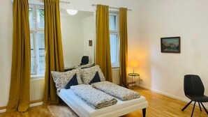 A bedroom with a bed, curtains, a chair, a lamp, and a painting on the wall.