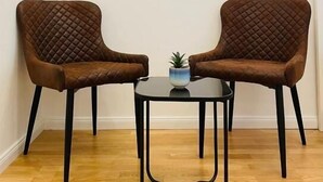 Two brown upholstered chairs with a quilted pattern, a small round table with a black metal base, and a framed picture on the wall.
