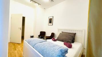 Un dormitorio con cama, una silla, una mesita de noche y una puerta.