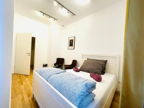 A bedroom with a bed, a chair, a bedside table, and a door.