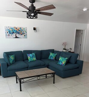 Ein Wohnzimmer mit Ecksofa, Couchtisch, Deckenventilator und Wandbild.