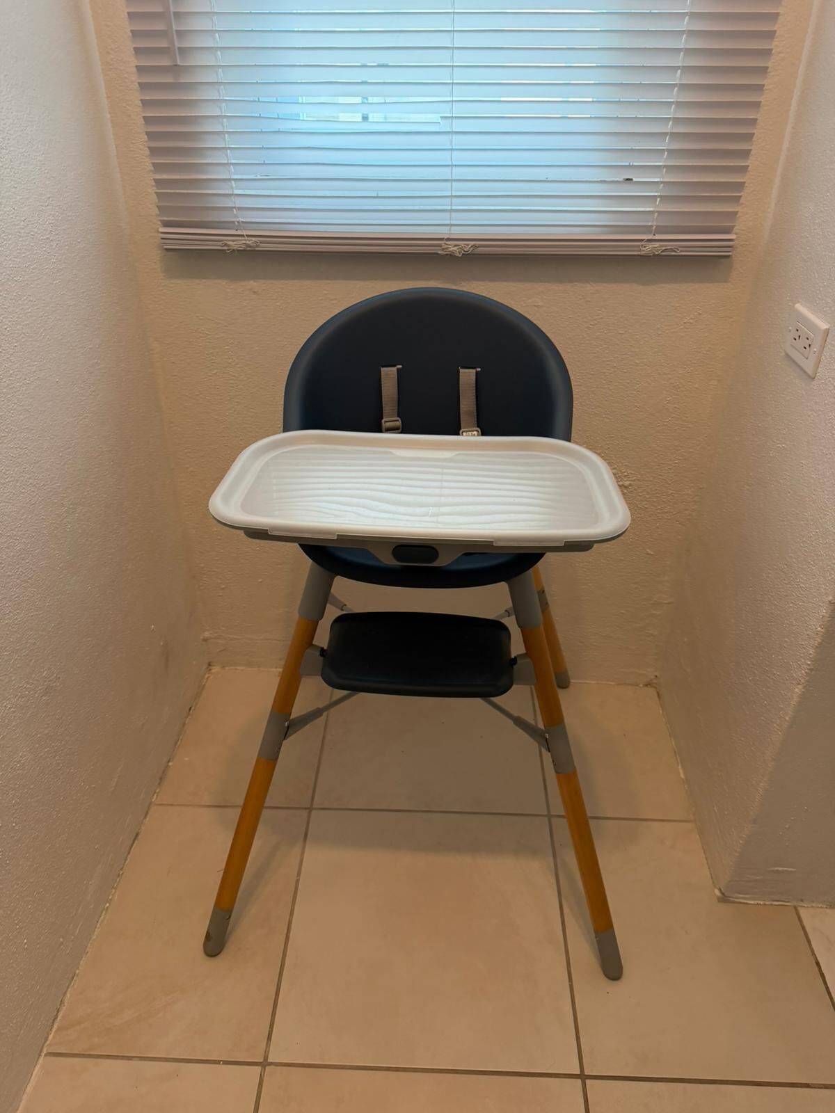 Una trona con bandeja, ubicada en un rincón con un ventanal arriba.