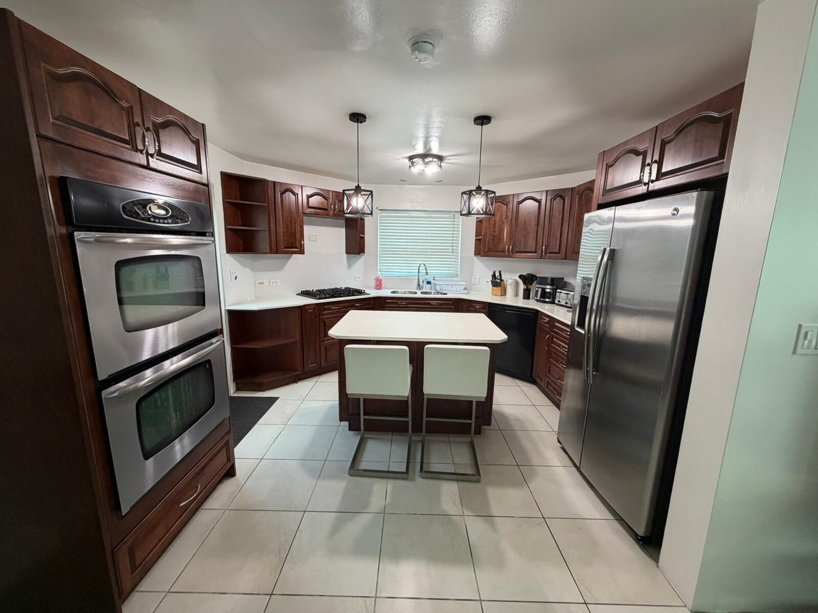 A modern kitchen with wooden cabinets, stainless steel appliances, a central island, and pendant lighting.