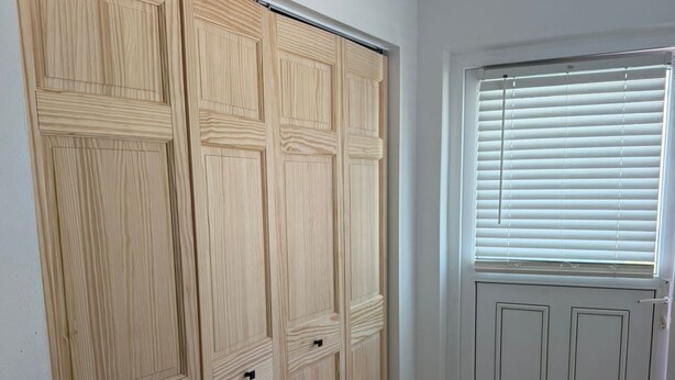 Ein Flur mit einem Holzschrank, einer Tür mit Fenster und einem gefliesten Boden.