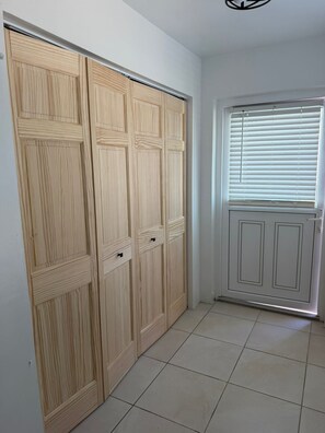 A hallway with a wooden wardrobe, a door with a window, and a tiled floor. - 2 Bedroom Escape, Walk to Beach - 5 Min to city (Pembroke)