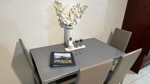 Ein Esstisch mit vier Stühlen, einer Vase mit weißen Blumen, einem Buch und einer Kaffeemaschine darauf.