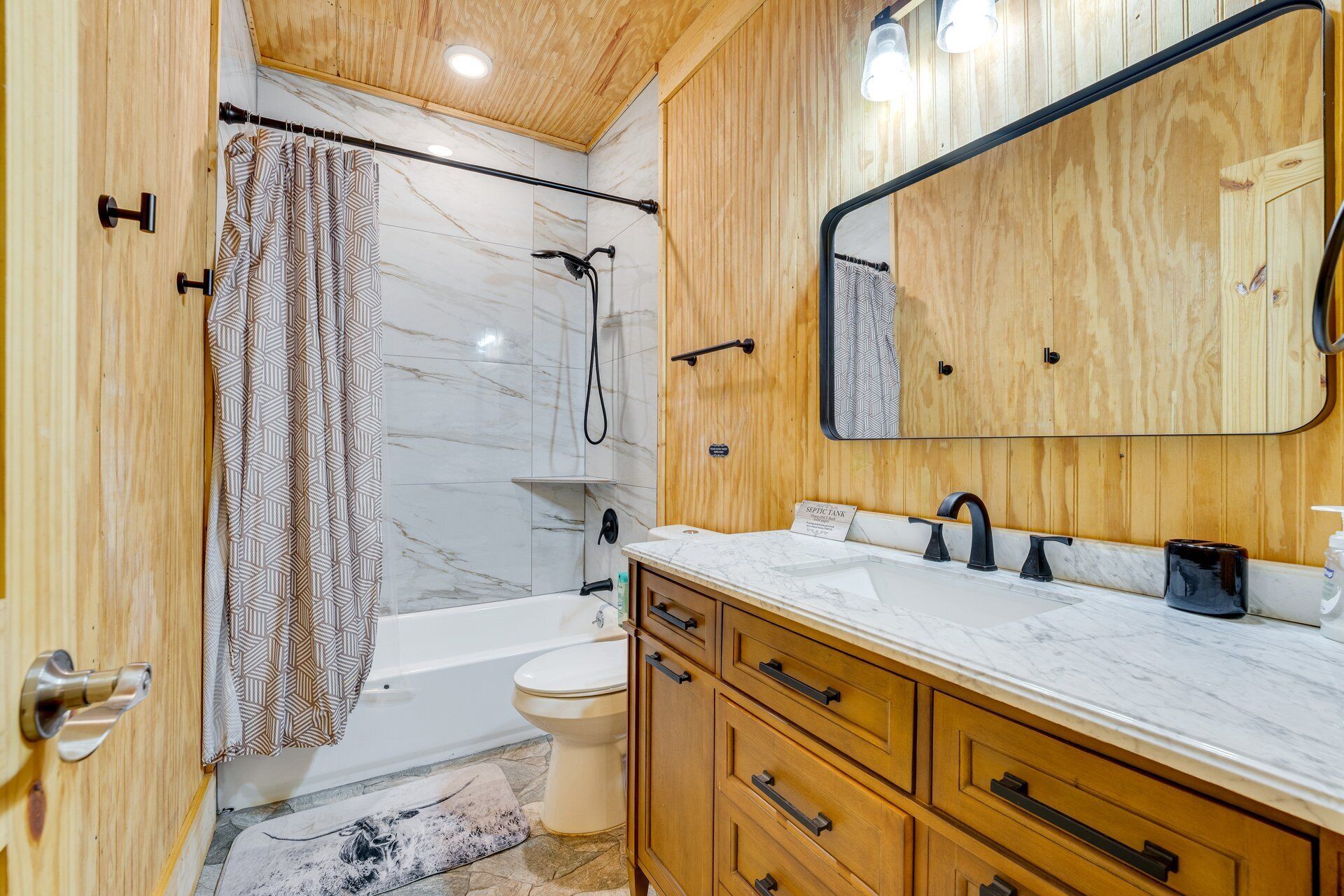 A bathroom with a shower, toilet, vanity, and a mirror.