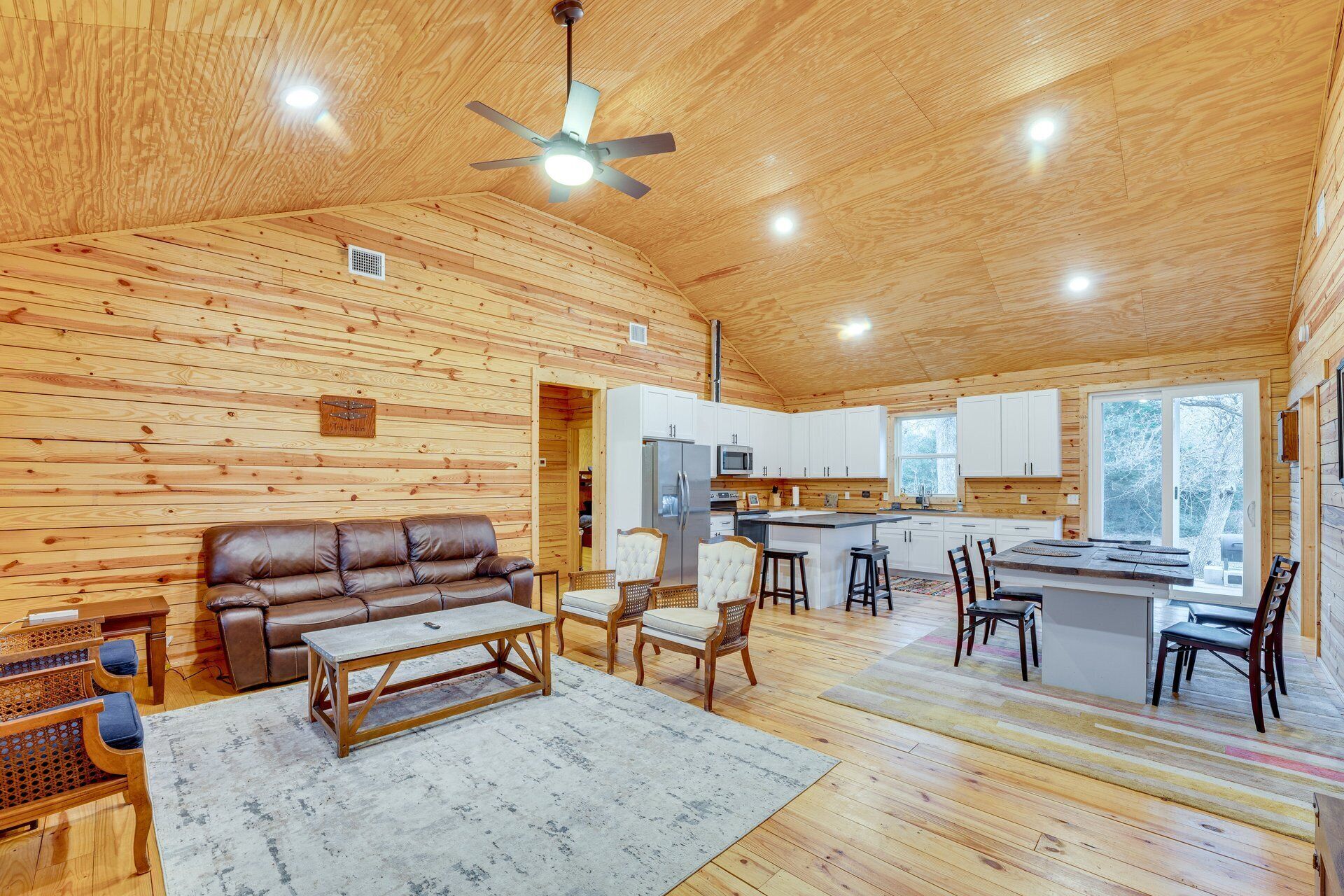 A spacious living room with a brown leather sofa, a wooden coffee table, and a ceiling fan.