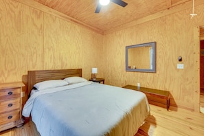 A wooden-paneled room with a bed, bedside table, lamp, and a mirror on the wall. - Private 10-acre Cabin Retreat! (Waelder)
