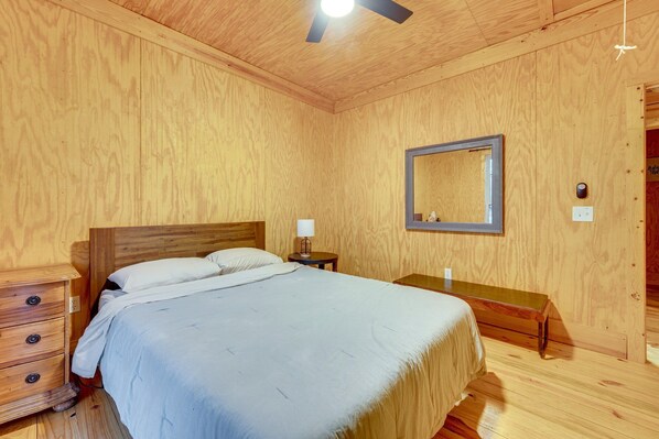 A wooden-paneled room with a bed, bedside table, lamp, and a mirror on the wall.