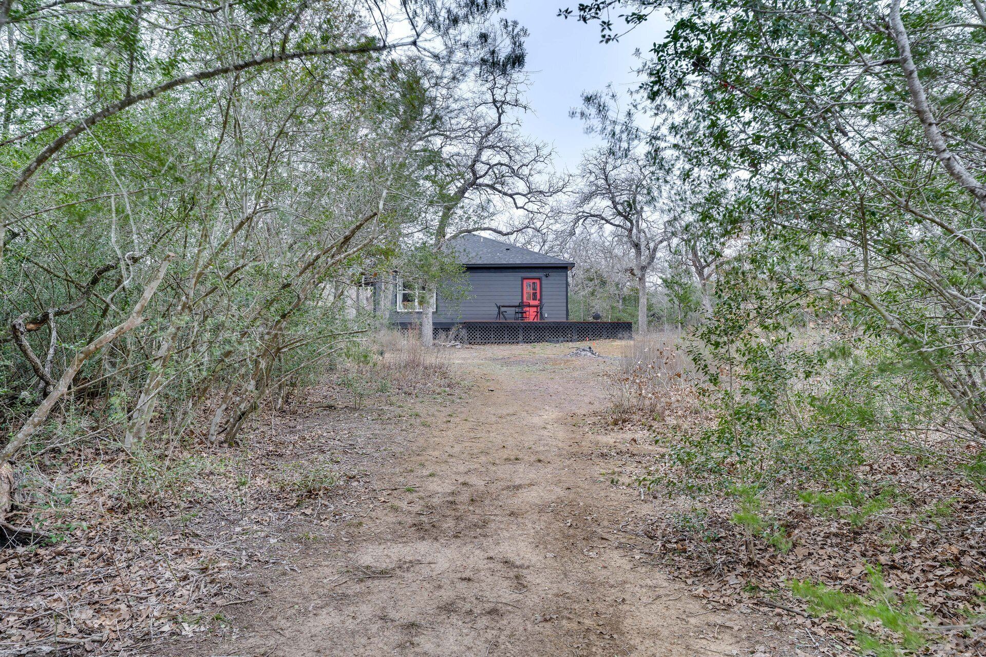 Une cabane avec une porte rouge, entourée d’une forêt dense et accessible par un sentier de terre.
