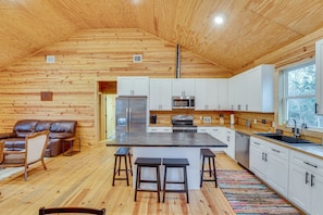 A cabin interior with a wooden interior, a kitchenette, a dining area with stools, and a leather sofa. - Private 10-acre Cabin Retreat! (Waelder)