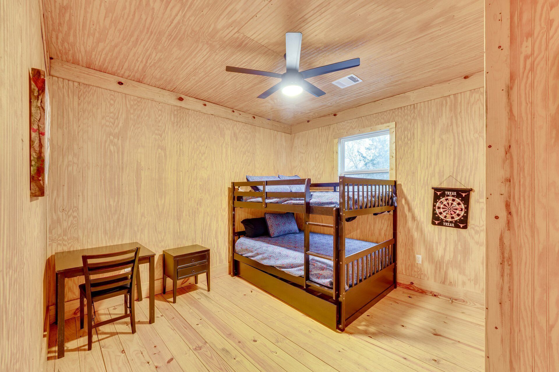 A wooden room with bunk beds, a desk, a chair, and a ceiling fan.