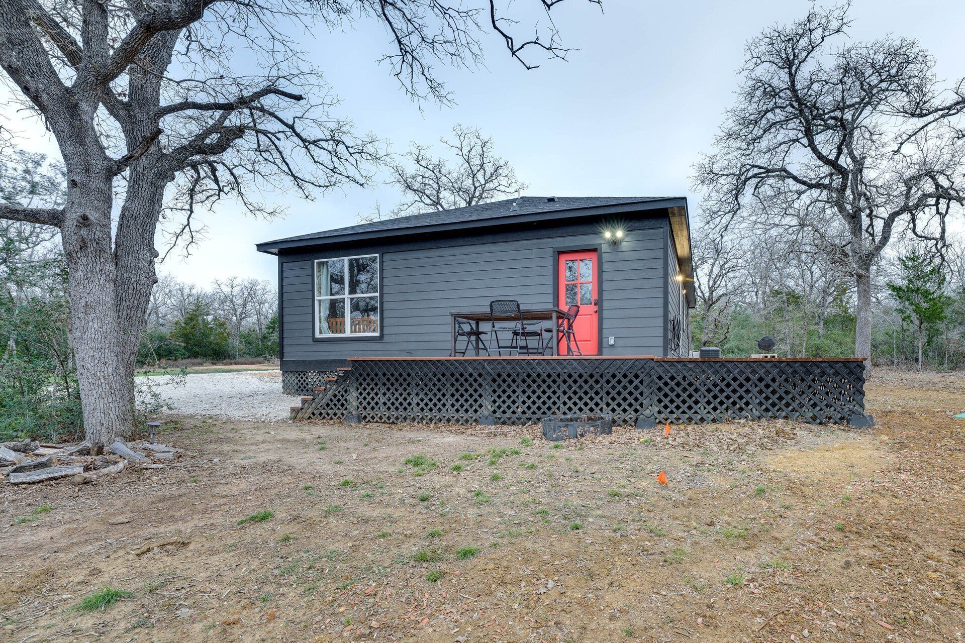 A small cabin with a red door, a window, and a patio area with a table and chairs.
