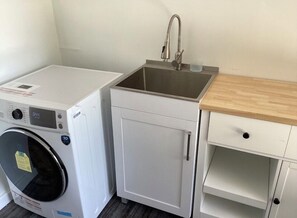 A compact laundry room with a washing machine, a sink, and a small cabinet. - Two bed room suite, ground floor, south facing down town city and garden view, (West Vancouver)