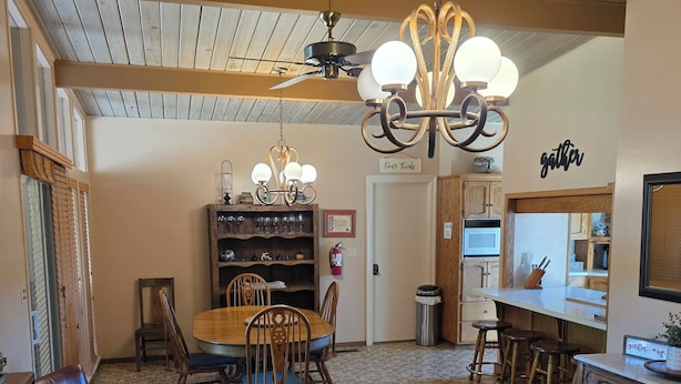 Un comedor acogedor con mesa y sillas de madera, una lámpara de araña y una cocina con microondas y taburetes de bar.