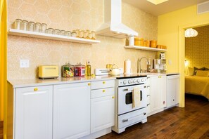 A kitchen with white cabinets, a stove, and a toaster. There are jars on a shelf and a coffee maker on the counter. - Hollyhock Suite 313: 5 beds/2 bath (Louisville)