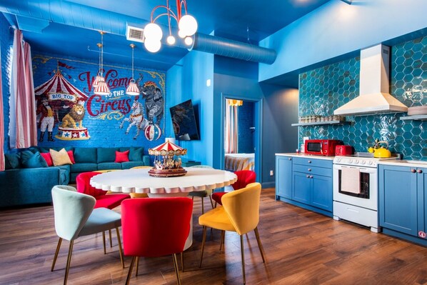 A vibrant room with a carousel table, blue walls, and a circus-themed mural. - Hollyhock Suite 313: 5 beds/2 bath (Louisville)
