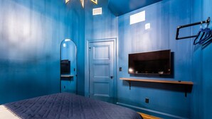 Ein Zimmer mit einem Bett, einem an der Wand befestigten Fernseher, einer Tür und einem Spiegel.