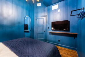 A room with a bed, a television mounted on the wall, a door, and a mirror. - Hollyhock Suite 310: 2 beds/1 bath (Louisville)