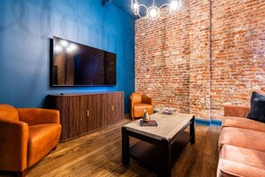 Ein Zimmer mit Backsteinwand, einem an der Wand befestigten Flachbildfernseher, einem Holzschrank und zwei Ledersofas.