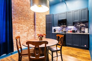 A kitchen with dark cabinets, a brick wall, and a round wooden table with chairs. - Hollyhock Suite 310: 2 beds/1 bath (Louisville)