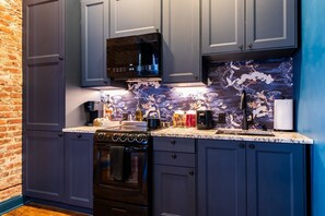 A kitchen with dark blue cabinets, a black microwave, and a tiled backsplash with a floral pattern. - Hollyhock Suite 310: 2 beds/1 bath (Louisville)