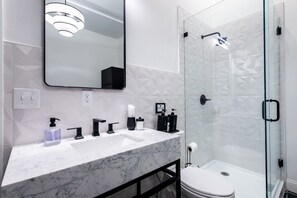 Ein modernes Badezimmer mit Marmorwaschtisch, schwarzen Armaturen, einer Duschkabine aus Glas und einer Toilette.