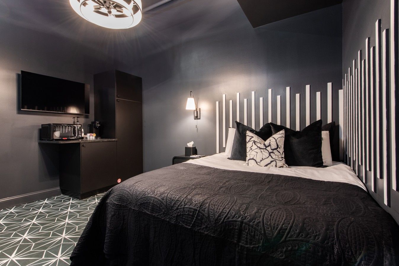 A modern hotel room with a large bed, a flat-screen TV, a small kitchenette, and a unique wall design.
