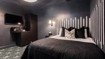 Una habitación de hotel moderna con una cama grande, un televisor de pantalla plana, una kitchenette pequeña y un diseño de pared único.