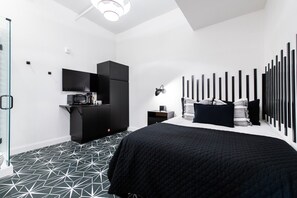 Ein modernes Schlafzimmer mit einem großen Bett, einem eingebauten Kleiderschrank, einer kleinen Küchenzeile und einer Duschkabine aus Glas.
