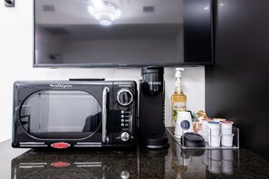 Eine Küchenzeile mit einer nachträglich installierten Mikrowelle, einer Kaffeemaschine, einer Flasche Alkohol und einem Kaffeezubereiter.
