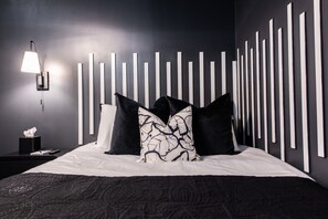 Une chambre à coucher moderne avec un grand lit, une table de chevet avec une lampe et un mur orné de panneaux verticaux.