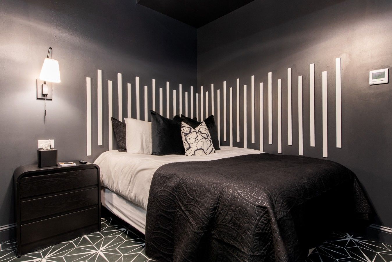 Un dormitorio moderno con cama, mesita de noche, lámpara y suelo con estampado geométrico.