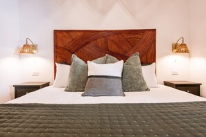 A neatly made bed with a quilted green bedspread, a wooden headboard with a geometric pattern, and two bedside lamps with a woven shade. - Hollyhock Suite 307: 3 bed /2 bath (Louisville)