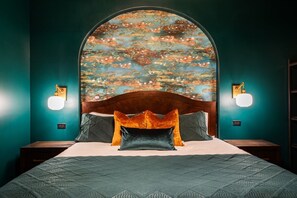 A bed with a headboard, two wall sconces, and a textured bedspread. - Hollyhock Suite 311: 1 bed/1 bath (Louisville)