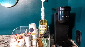 Keittiön työtasolla on kahvinkeitin, pullo Monin-merkkistä vaniljansokerisiirappia sekä läpinäkyvä muovinen säilytysastia, jossa on erilaisia mausteita ja keittiövälineitä.