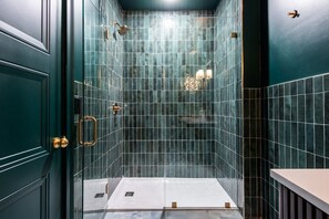 A bathroom with a tiled shower area, a door with a handle, and a light fixture. - Hollyhock Suite 311: 1 bed/1 bath (Louisville)