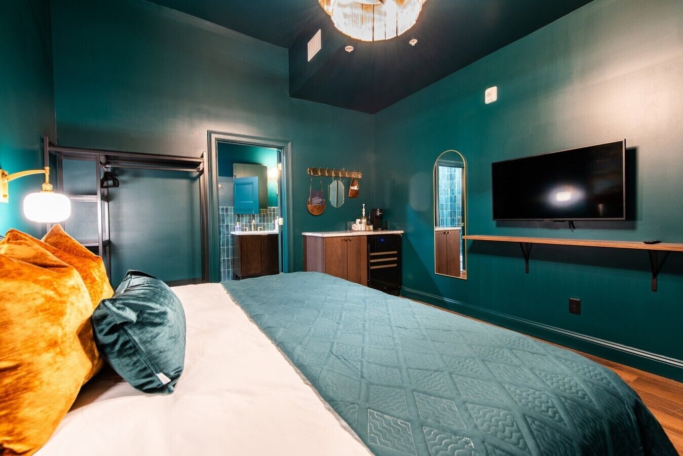 Ein Schlafzimmer mit Bett, Fernseher, Spiegel und einem durchgehenden Türrahmen sichtbaren Badezimmer.