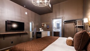Ett hotellrum med en säng, en tv, en spegel, ett handfat och en dörr.