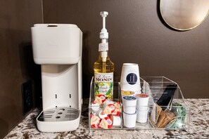 Eine Kaffeemaschine, eine Flasche Monin French Vanilla Sirup und eine Aufbewahrungsbox mit verschiedenen Gewürzen auf einer Marmorarbeitsplatte.