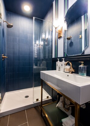 A modern bathroom with a white sink, gold fixtures, and a glass-enclosed shower. - Hollyhock Suite 308: 2 beds/1 bath (Louisville)