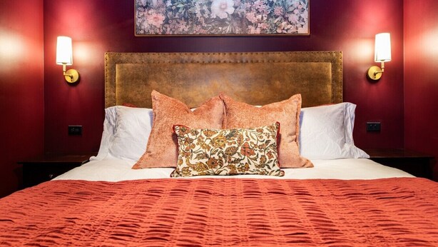 Ein Hotelzimmer mit einem großen Bett, roten Wänden, einem Blumenbild über dem Bett und Wandlampen.