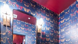 Ein Badezimmer mit einem weißen Waschbecken, goldenen Armaturen und einer Toilette. Die Wände sind mit einem Schmetterlingsmuster verziert.