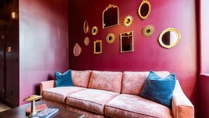 Ein Zimmer mit roter Wand, einem rosafarbenen Sofa mit blauen Kissen und einem Holztisch mit Büchern und einem dekorativen Gegenstand.
