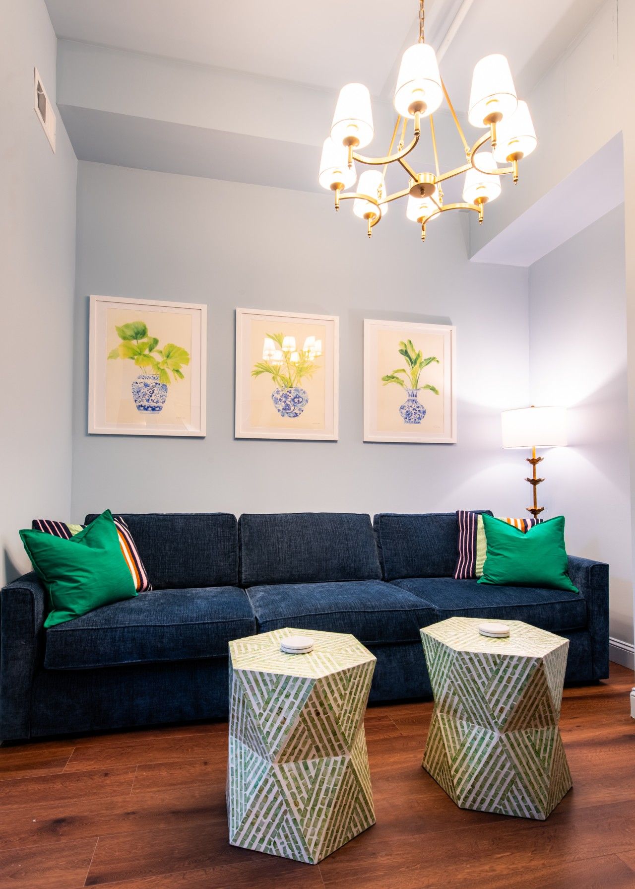 Une pièce avec un canapé bleu foncé, des coussins verts et deux petites tables d’appoint à motifs.