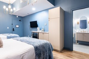 A hotel room with two beds, a minibar, a television, and a bathroom with a mirror and sink. - Hollyhock Suite 306: 1 bed + 1 loft bed/1 bath (Louisville)